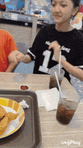 a girl wearing a black shirt with the number 1 on it sits at a table