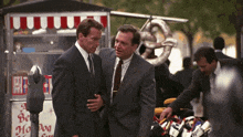 two men in suits are standing in front of a hot dog stand