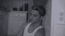 a man in a white tank top leans against a wall