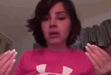 a woman is wearing a pink under armour shirt and holding her hands up in the air .