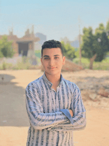 a young man in a striped shirt with his arms crossed smiles for the camera