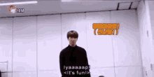 a man in a black sweater is standing in front of a wall and talking to someone .