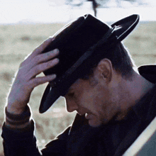 a man wearing a black cowboy hat is adjusting it .