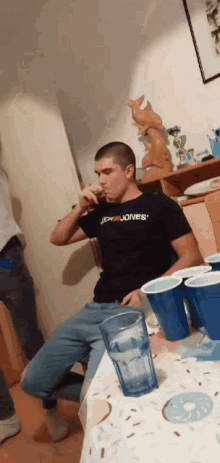 a man wearing a black shirt with the word jones on it drinks a beer