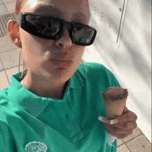 a woman wearing sunglasses and a green polo shirt is holding an ice cream cone