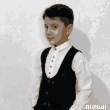 a young boy wearing a black vest and white shirt is standing in front of a wall with the name aliabdi on it