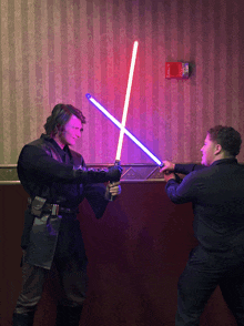 two men are fighting with lightsabers in front of a wall that has a fire extinguisher on it