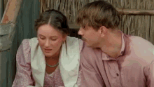 a man and a woman are sitting next to each other and talking . the woman is wearing a pink dress .