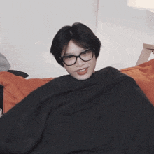 a young man wearing glasses is wrapped in a black blanket and smiling
