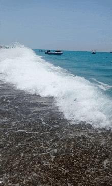 waves crashing on a beach with boats in the background