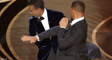 two men in suits and bow ties are fighting on a stage with the words imgflip.com in the lower right corner