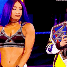 a woman with purple hair is standing next to a man holding a championship belt ..