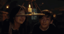 a boy and a girl are looking up at a candle hanging from a chandelier in a dark room .
