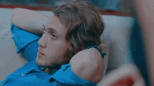 a young man in a blue shirt is sitting on a couch and looking up .