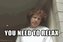a man with curly hair is standing next to a wall and says you need to relax