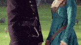 a man in a black suit and a woman in a blue dress are standing next to each other on a grassy field .