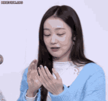 a woman wearing a blue sweater is clapping her hands in front of a microphone ..