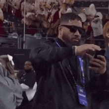 a man wearing sunglasses and a lanyard is taking a picture of himself with his cell phone .