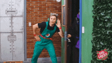 a man in green overalls is standing in front of a door that says " gato galinha " on it