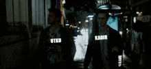two men are standing next to each other in front of a bus with the words utku and kadir written on their faces .