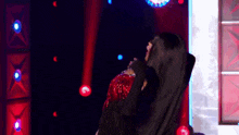 a woman in a black dress is dancing on a stage with red lights behind her .