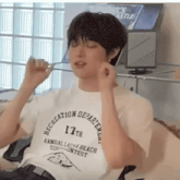 a man wearing a recreation department shirt holds a spoon in his mouth