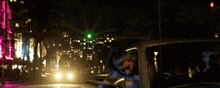 a woman sits in a car at night with a neon sign that says ' miami ' on it
