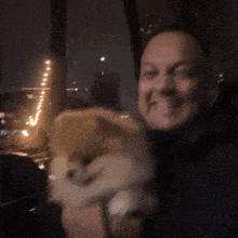 a man is smiling while holding a small dog in his arms