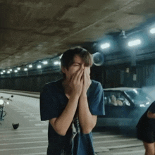 a young man in a blue shirt is covering his face with his hands