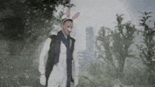 a man wearing bunny ears and a scarf stands in a forest
