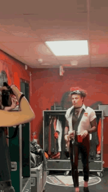 a man is standing in a dressing room holding a red cup and a guitar .