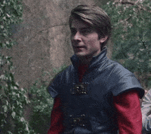 a man wearing a blue vest and a red shirt is standing in a forest