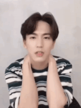 a young man wearing a striped shirt is sitting down with his hands on his neck .