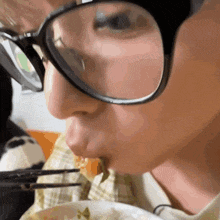 a close up of a person wearing glasses eating something with chopsticks
