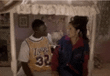 a man and a woman are standing next to each other in a room . the man is wearing a lakers jersey .