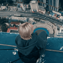 a woman sits on the edge of a building looking down at the city
