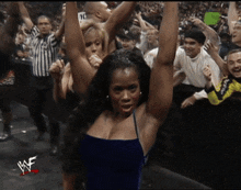 a woman in a blue dress stands in front of a crowd with her arms in the air and the word wwe on the bottom right