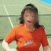 a woman wearing an orange adidas shirt stands in front of a tennis net