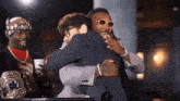 a man wearing sunglasses hugging another man in a suit