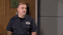 a man in a blue shirt is sitting in front of a wooden wall with a sign that says hhh .