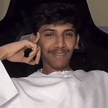 a man in a white shirt is sitting in a chair with his hands on his face .