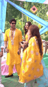 a man in a yellow shirt is standing next to two women in yellow dresses