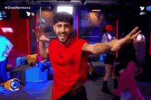 a man in a red shirt is dancing with his arms outstretched in a club