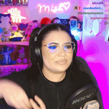a woman wearing headphones and glasses is holding a rode microphone in front of a neon sign that says misky