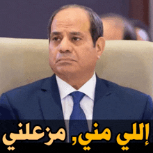 a man in a suit and tie sits in a chair with arabic writing below him