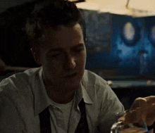 a man in a white shirt and tie is drinking a glass of water