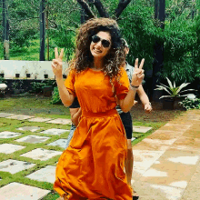 a woman wearing an orange dress and sunglasses giving a peace sign