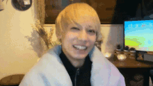 a man with blonde hair is smiling in front of a tv screen