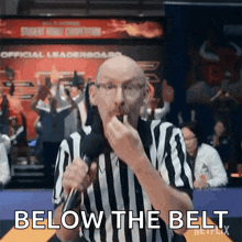 a referee in a striped shirt is holding a microphone and says below the belt