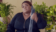a woman in a black dress is holding a sword in front of potted plants ..